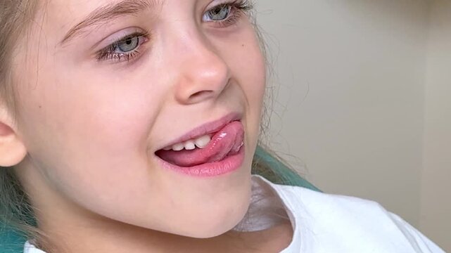 Little girl with brown hair sits in a chair, sticking out her tongue and doing exercises with her tongue at a speech therapist's appointment. Training pronunciation concept. High quality footage