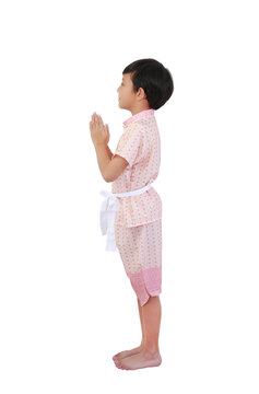 Charming young Asian boy dressed in traditional pink Thai costume performing the "Wai," a respectful Thai greeting gesture, while standing against white background. Side view.