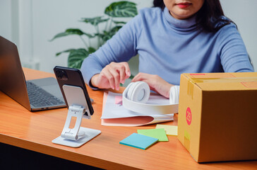 entrepreneur packing product box at office with smartphone, laptop representing ecommerce business, online selling, order fulfillment, small business workflow digital marketing startup