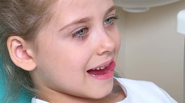 Little girl with brown hair sits in a chair, sticking out her tongue and doing exercises with her tongue at a speech therapist's appointment. Training pronunciation concept. High quality footage