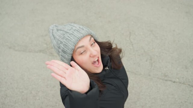 Joyful woman dancing. Woman wearing beanie joyfully dancing with friendly wave. Cheerful woman sporting beanie happily dancing while waving to camera complimented by lively facial expressions