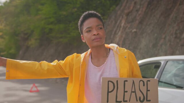 Hiker signals for ride by vehicle. Man in yellow coat asks for transportation. Faint sunlight illuminates stranded traveler requesting ride on peaceful countryside path