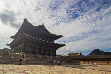 Fototapeta premium Majestic Korean palace architecture with symmetrical stone courtyard and layered tiled roof under dramatic sky, traditional Asian heritage landmark, cultural travel destination concept