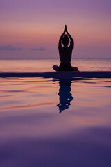 beautiful silhouette of woman practicing yoga outside with reflection in water, body mind soul harmony