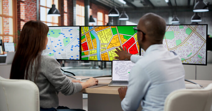 Two GIS Analysts In Office Using Computers To Review Urban Planning Maps
