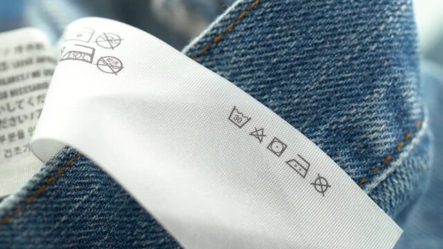 Close up of clothing care label on denim fabric with washing symbols.