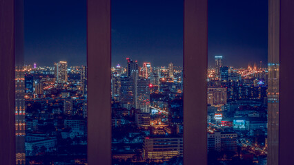 Obraz premium Stunning night cityscape of Bangkok through vertical window frames featuring glowing city lights