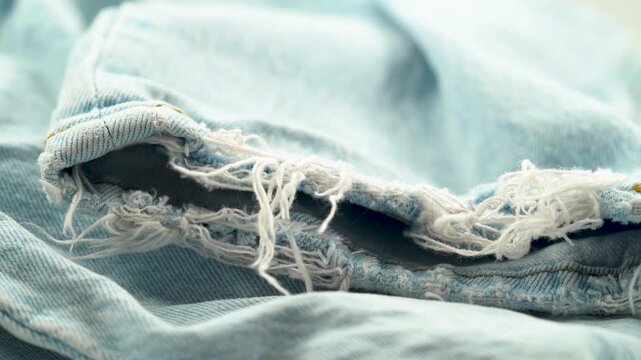 Close up of frayed denim hem with loose threads and worn edges.