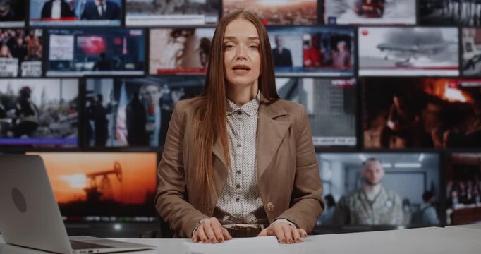 Female Anchor Hosts Prime Time News in High Tech Studio Equipped With Large Media Wall of Live Feeds. Woman Addresses Viewers With Authority. Trusted Journalism and Global Communication Network.