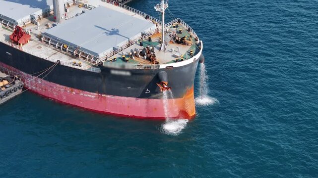 large cargo ship's bow discharging ballast water into the ocean. Maritime engineering operations, industrial shipping logistics, and environmental maintenance at sea.
