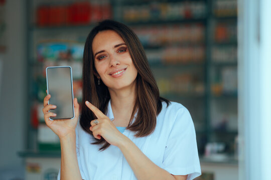 Smiling Pharmacist In Uniform Pointing Finger At a Phone Display. uhappy pharmacy professional assistant showing a mobile phone