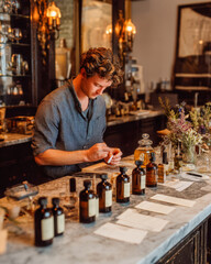 Artisan Perfumer Testing Scent Strip with Glass Bottles and Paper Labels in Elegant Studio