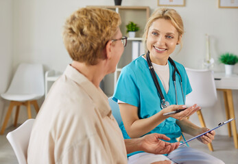 Obraz premium Conversation of smiling nurse and happy elderly patient in modern clinic. Medical consulting of doctor with stethoscope and clipboard during appointment, professional healthcare examination