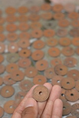 Fingers Holding a Vintage Holed Coin Above a Currency Pile © Mas