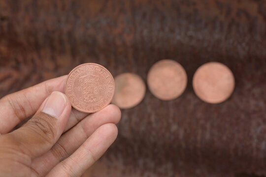 Vintage Dutch East Indies Coin Held in Hand Against Rusted Metal Background