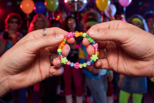 Hands holding a colorful beaded bracelet with a disco party background