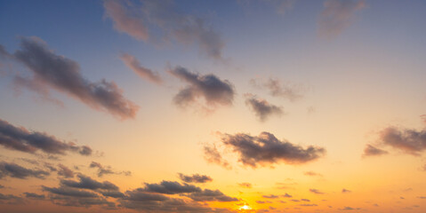 Obraz premium Beautiful golden sunset sky with scattered clouds at twilight,A breathtaking wide-angle shot of a vibrant sunset sky, featuring a gradient of golden orange, yellow, and deep blue hues.