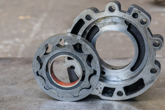 Close-up of a disassembled automatic transmission oil pump gerotor set with metal housing. Detailed view of internal gear assembly and hydraulic components on a steel workshop table.