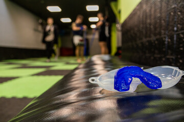 Blue mouthguard placed on gym bench with athletes approaching in the background, symbolizing readiness for intense training sessions and importance of safety in sports.