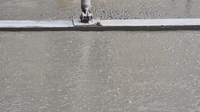 Close-up of wet concrete being smoothed with a trowel, front view, tool moving backwards.