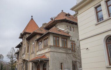 Obraz premium Architectural detail of a traditional Romanian villa in Bucharest featuring a distinctive red-tiled roof, stone facade, and classical window designs