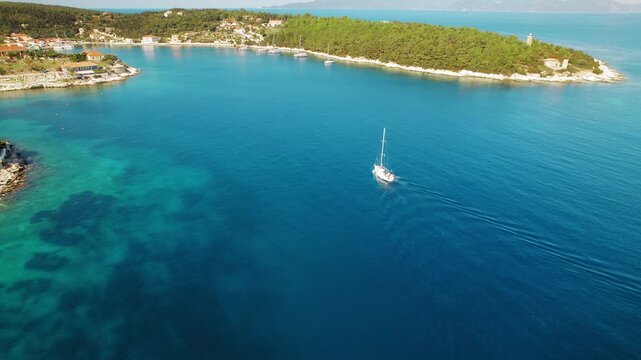 Sailing boat entering tranquil harbor with coastal village on Kefalonia island Greece