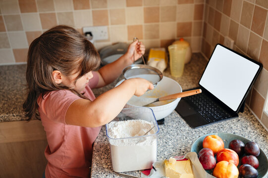 Girl adding flour to the bowl, home baking with technology.
