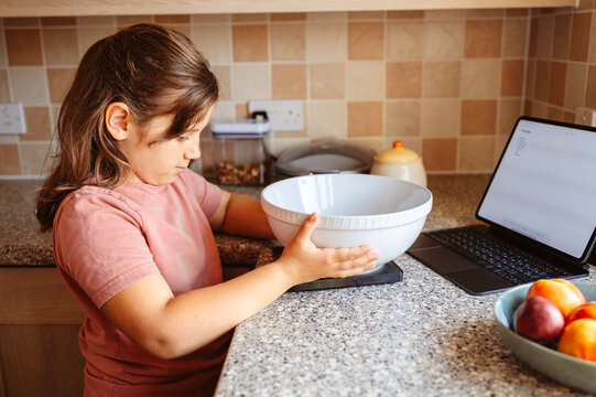 Child girl putting bowl on the kitchen scales during baking pie.