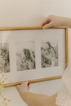 Hands hanging framed family portraits on wall