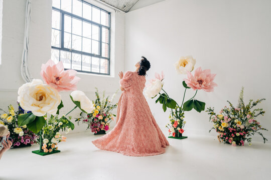 Dancer in flowing pink gown twirling among oversized flowers