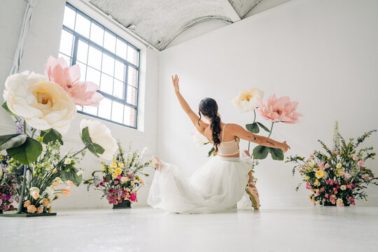 Ballet dancer seated pose among oversized flowers in studio