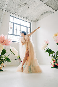 Ballerina in long tulle dress dancing among giant flowers
