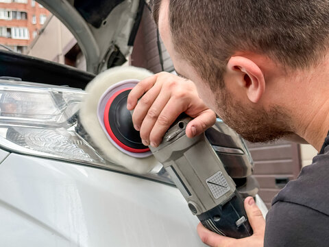  Man polishes the glass of a  headlight with a polishing machine from small scratches and chips. Hands of male professional worker with orbital polisher, polishing car headlight. 
