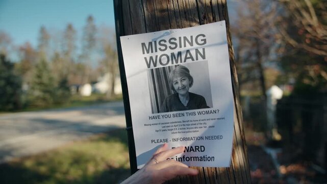 Hands removing missing woman poster from wooden utility pole on suburban street suggesting disappearance or investigation update