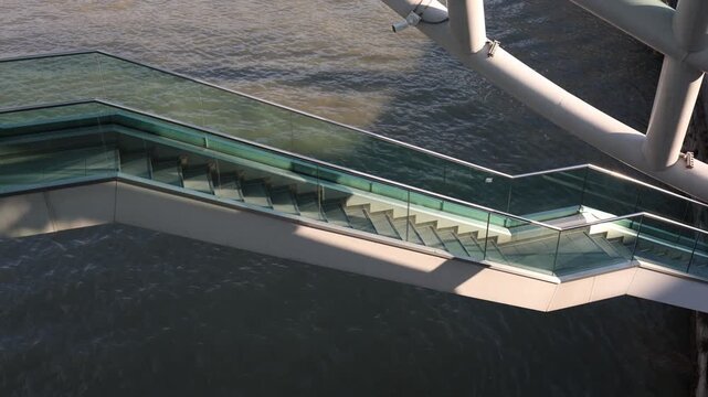 Modern glass staircase above river with strong geometric perspective and structural lines transparent design meets flowing water creating contrast between architecture and natural movement