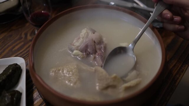 Rich meat broth soup with bone served in rustic bowl spoon lifts tender piece traditional comfort food warm dining table authentic home style meal