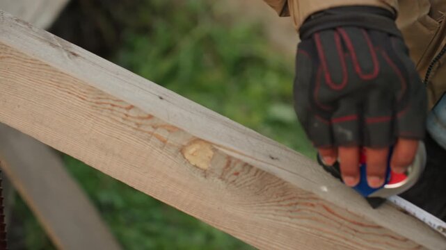 Contractor measuring cut line for repair, gloved hand extends tape over plank and marks precise point for cut, closeup of measurement process, urgent handson fix during outdoor renovation at worksite,