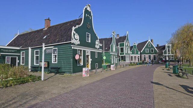 Traditional green wooden houses and brick path at the Zaanse Schans museum village In Zaandam. Historic Dutch architecture under a clear blue sky.