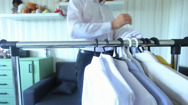 A man carefully hangs crisp white shirts on a clothing rack, emphasizing order, care, and the quiet ritual of preparing for the day with intention and dignity.