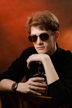 Elegant young man in sunglasses and black turtleneck with whiskey bottle.