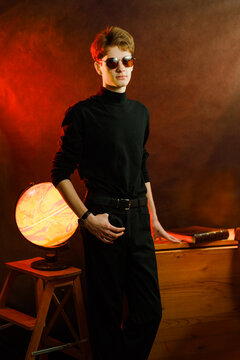 Fashion portrait of a teenager in black turtleneck and sunglasses with glowing globe dramatic red lighting.