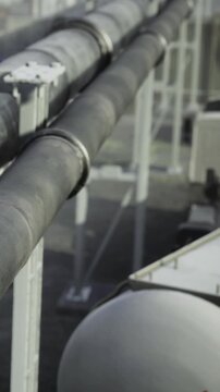 Pipes are arranged in a row at an industrial site. They appear to be transporting substances and are positioned on metal supports. The setting is well lit by natural light.