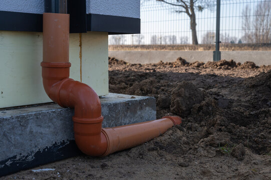 PVC sewer pipe connected to house downspout drainage at building foundation, outdoor rainwater drainage system installation.