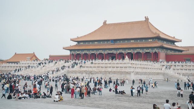 Crowded forbidden city courtyard asian tourists, photographers, families, guides ascend marble steps toward red imperial palace under overcast sky, wide composition captures scale, cultural heritage,