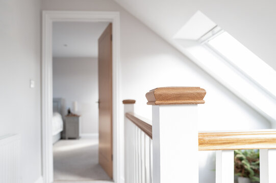 Shallow focus of a wooden banister in a newly completed first floor loft conversion for a bungalow. In the distance a door leads the way to a first floor bedroom.