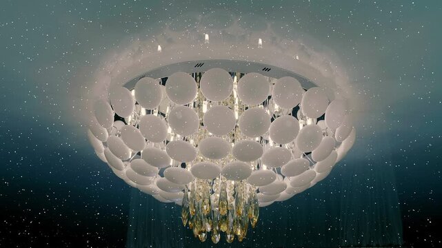 Beautiful modern fashionable ceiling chandelier sparkling with its glass elements on a white glossy ceiling. View through sparkling particles. Shot in motion