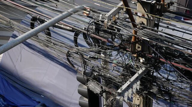 Chaotic tangle of electrical and fiber optic cables on a utility pole in a crowded urban street in Southeast Asia