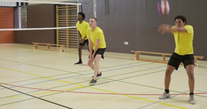 Diverse male team in yellow tops receiving near-side serve, drilling bumps and digs with volleyball