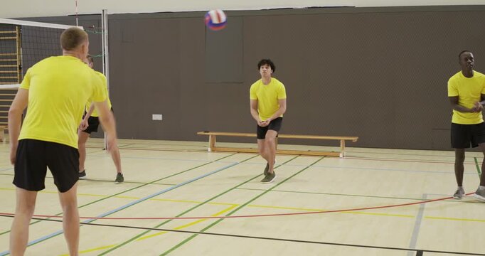Six male volleyballers in yellow shirts bumping incoming ball, digging, practicing defense in gym