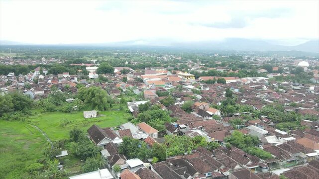 Aerial 4K view of a dense Indonesian suburban village with red-tiled roofs and distant mountains.